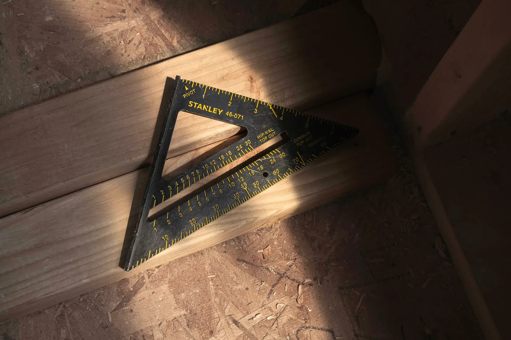 STANLEY 46-071 black speed square with yellow markings placed on wooden planks, angled view.