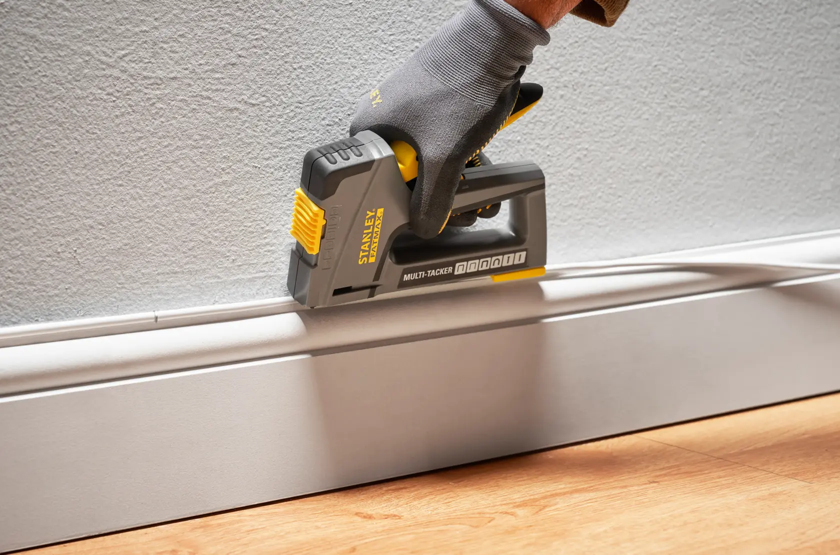 Photo of STANLEY FMHT6-70868 multi-tacker in use attaching trim to wall, held by gloved hand.
