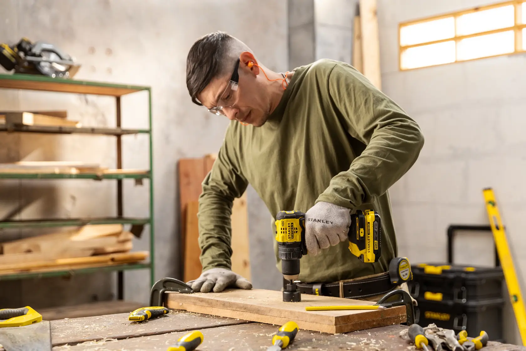 STANLEY SBD714 drill being used on wood in a workshop, with tools and clamps on the workbench.