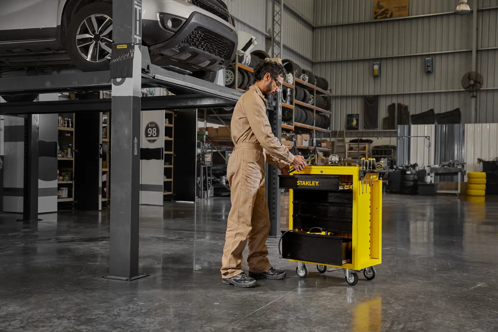 Photo of STANLEY STST98623LA yellow tool cart with open drawers in a workshop, mechanic standing beside it.