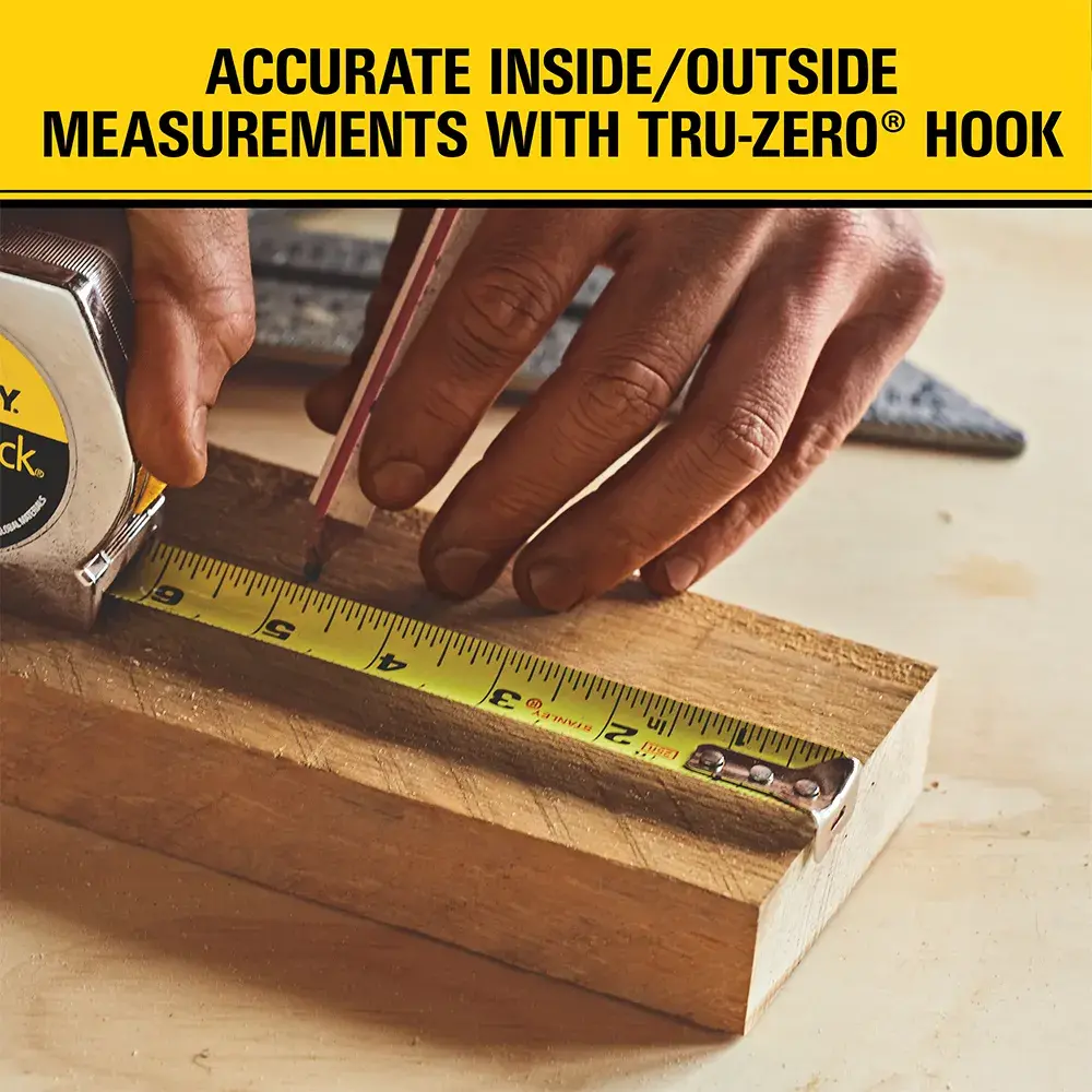 A close-up of a person using a Stanley measuring tape on a wooden block, with a pencil marking measurements. Text above reads: 'Accurate inside/outside measurements with Tru-Zero hook.'