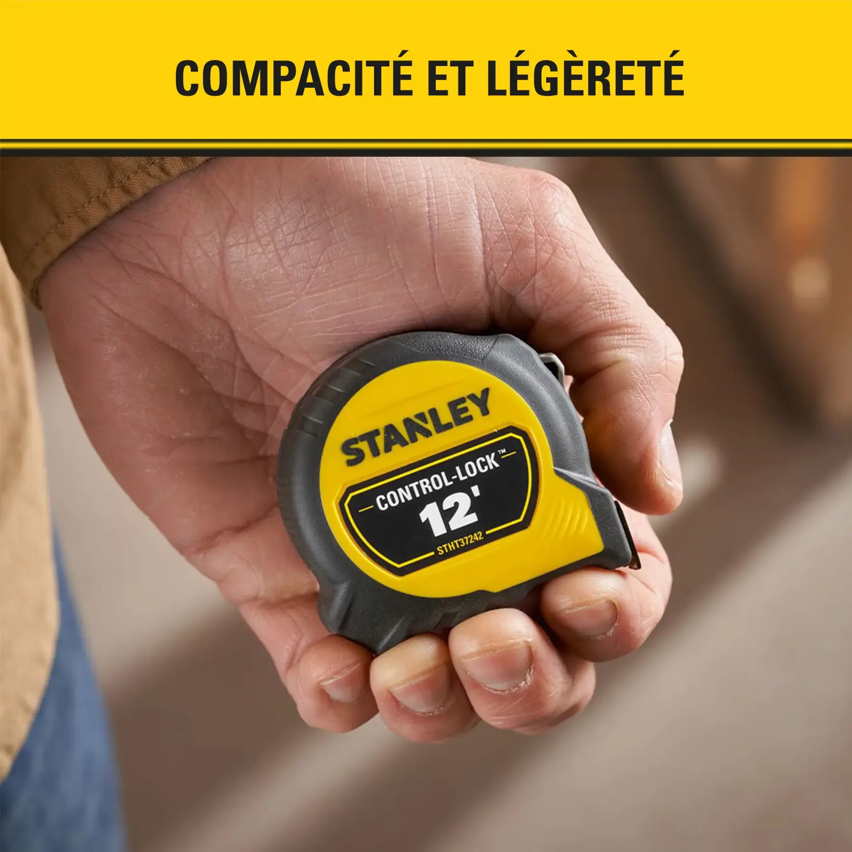 Une main tient un mètre ruban Stanley Control-Lock de 12 pieds, jaune et noir, modèle STHT37242. L’arrière-plan et la bannière jaune mettent en avant la compacité et la légèreté du produit.