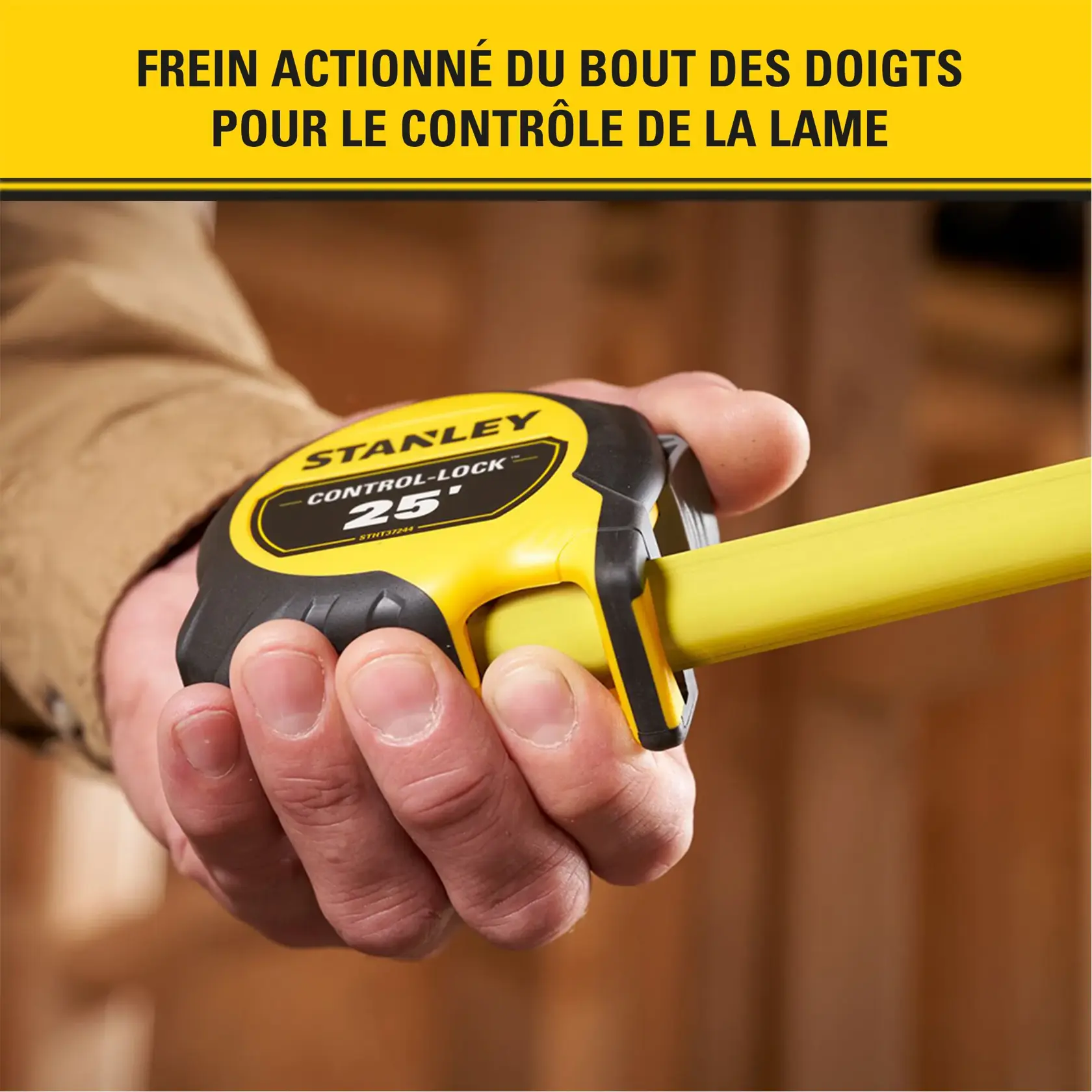 Gros plan sur une main tenant un mètre ruban Stanley Control-Lock de 25 pieds avec le ruban jaune déployé. L'arrière-plan est un intérieur flou. Un texte en haut en français met en avant le frein actionné du bout des doigts pour le contrôle de la lame.