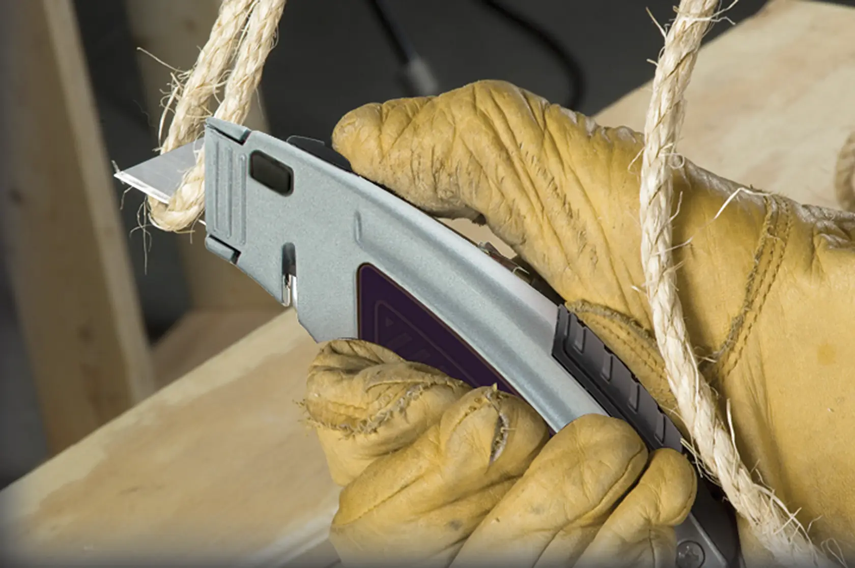 Photo of gloved hand using STANLEY 10-788 utility knife to cut thick rope on wood surface.
