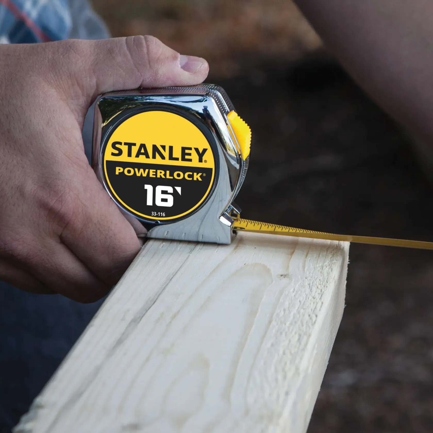 STANLEY 33-116 PowerLock tape measure in use measuring a wooden plank, close-up view.
