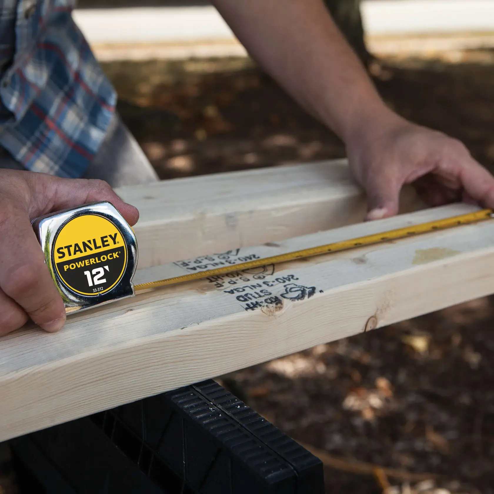 Stanley 33-312 tape measure being used to measure wood plank outdoors, close-up photography.
