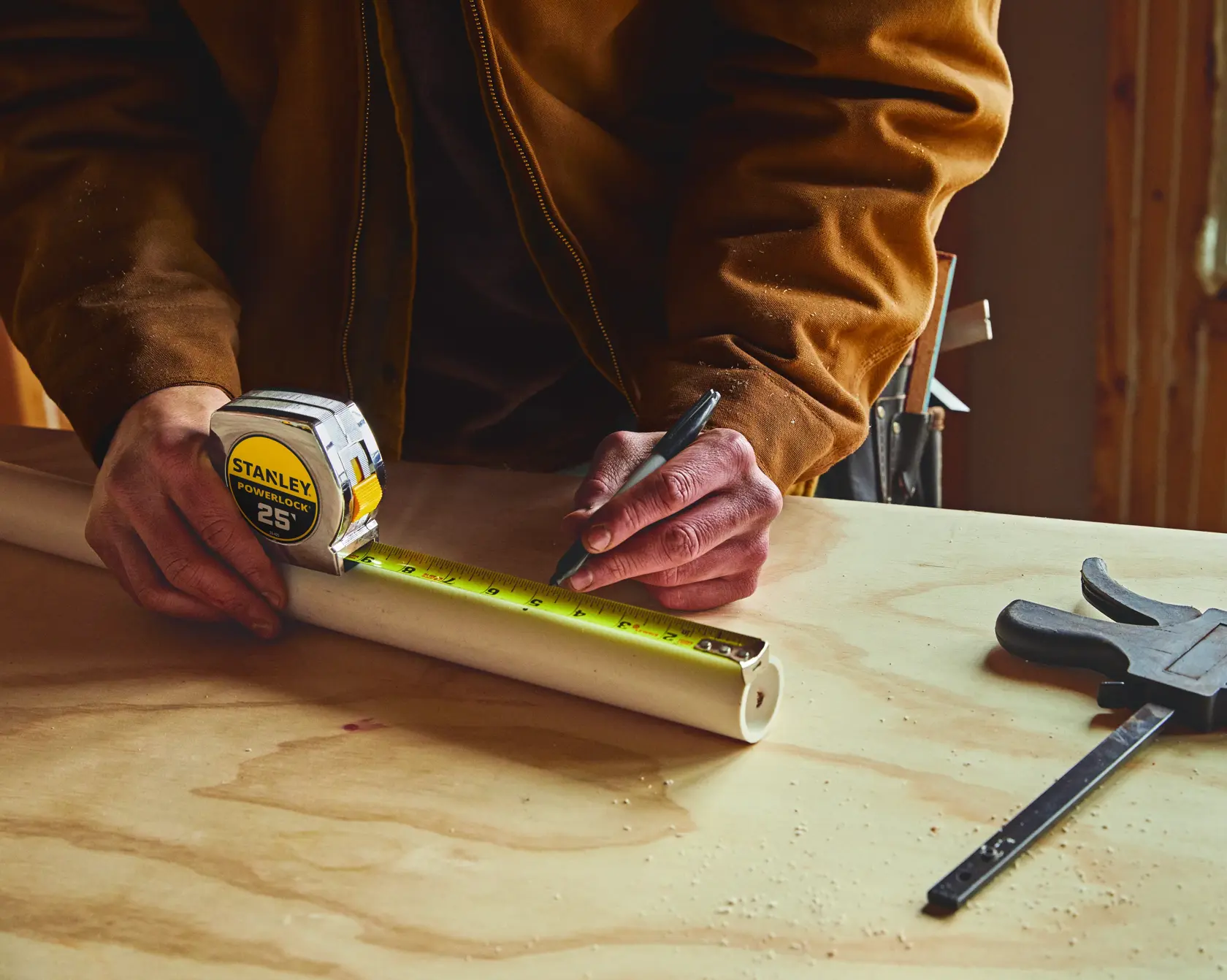 Stanley 33-425 PowerLock tape measure marking PVC pipe on workbench, photography close-up.
