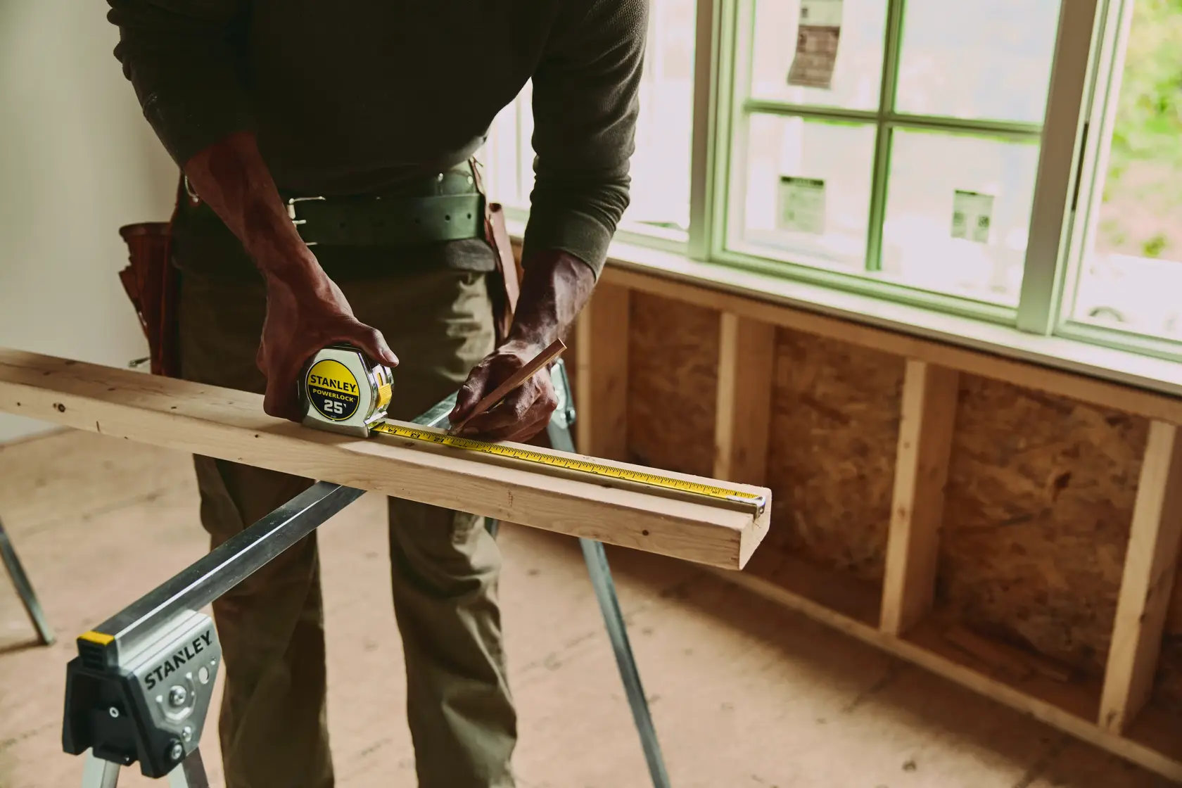 Photo of STANLEY 33-425 tape measure being used to mark a wooden board in a construction setting.