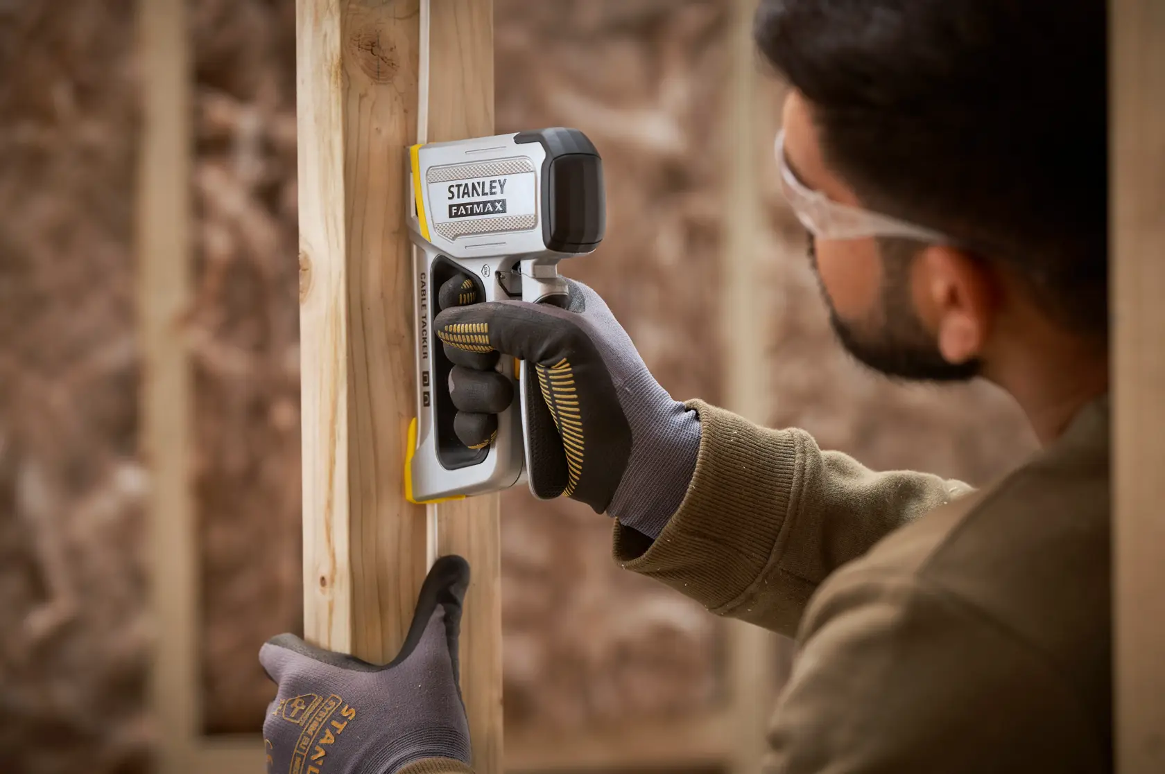Stanley FMHT70100 FATMAX stud finder in use against wooden framing, user wearing gloves.