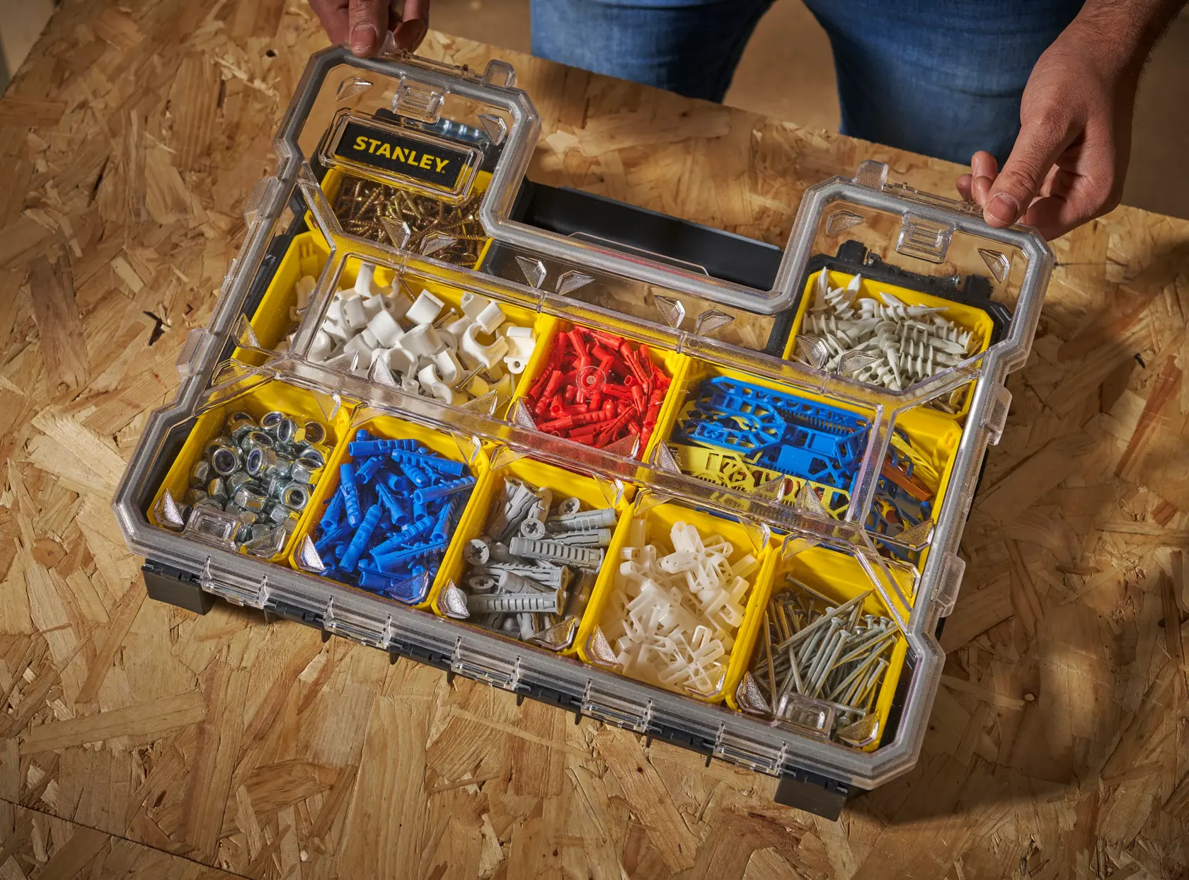 STANLEY FMST14820 organizer with clear lid holding assorted wall anchors and hardware in yellow compartments, angled top view.