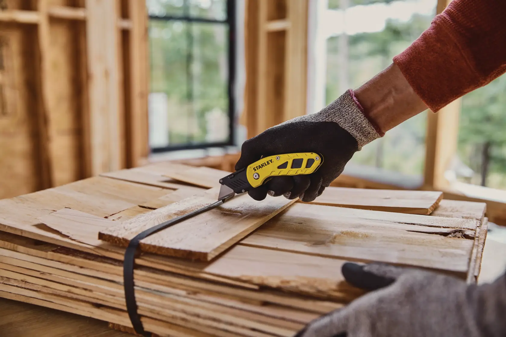 STANLEY STHT10424 utility knife with yellow and black handle in use cutting strap on stack of wooden boards.