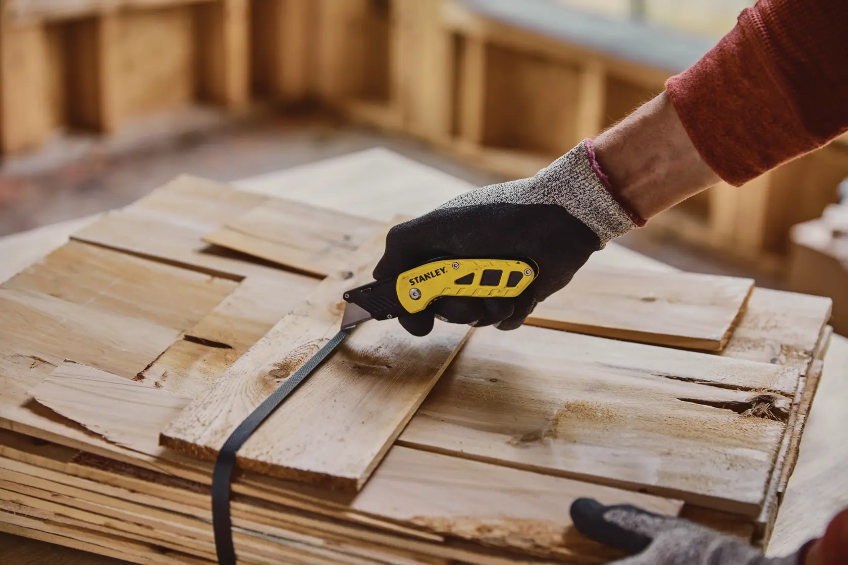 Photo of STANLEY STHT10424 utility knife cutting strapping on stacked wood boards in workshop.