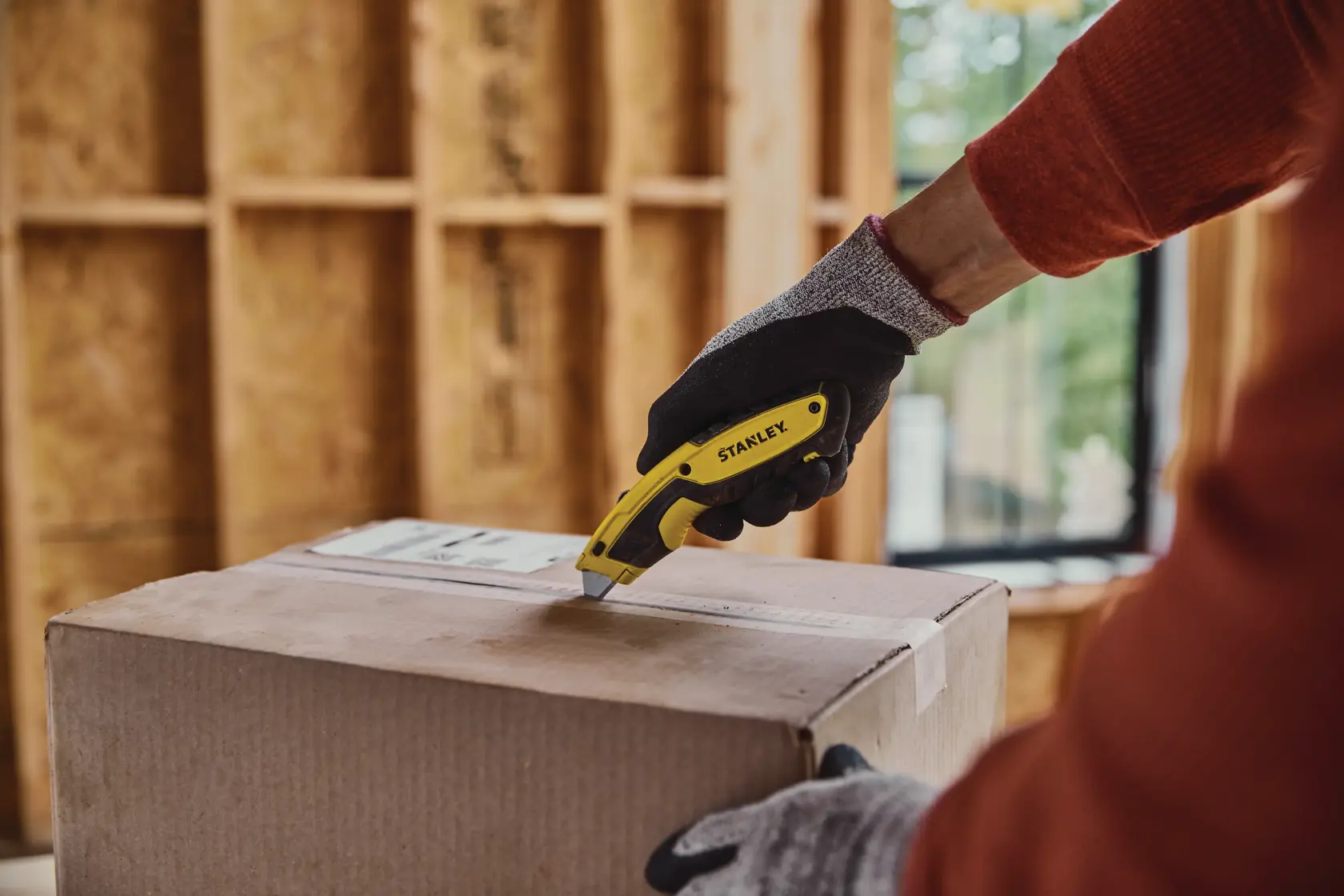 Stanley STHT10479 utility knife cutting a cardboard box, gloved hand holding the yellow tool.