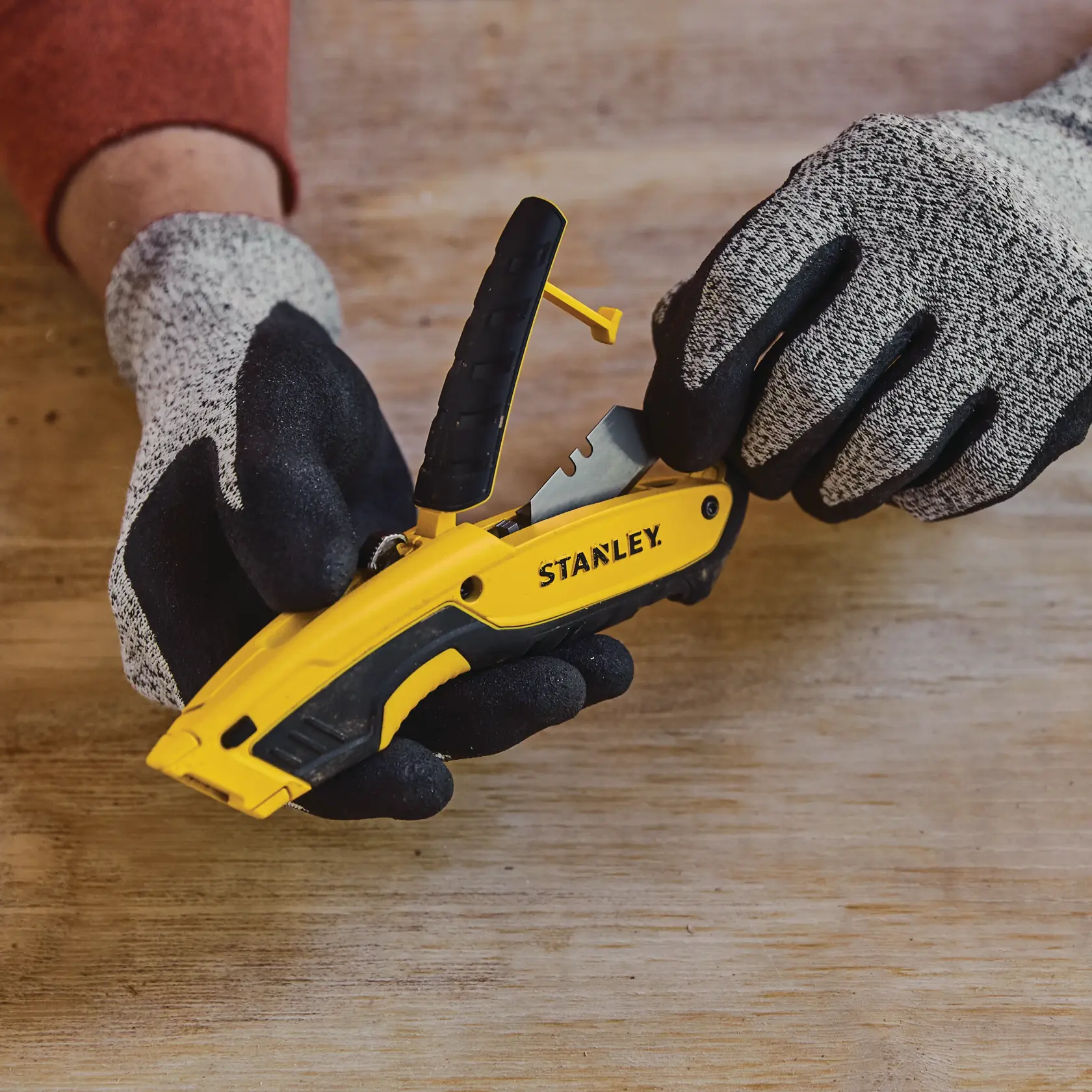 Photo of STANLEY STHT10479 yellow and black utility knife with gloves, shown during blade change on wood surface.