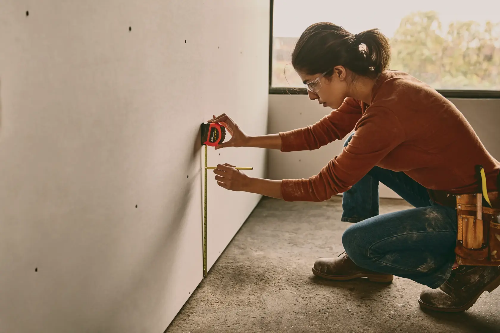 STANLEY STHT30817S tape measure in use measuring on drywall, person kneeling with tool belt.