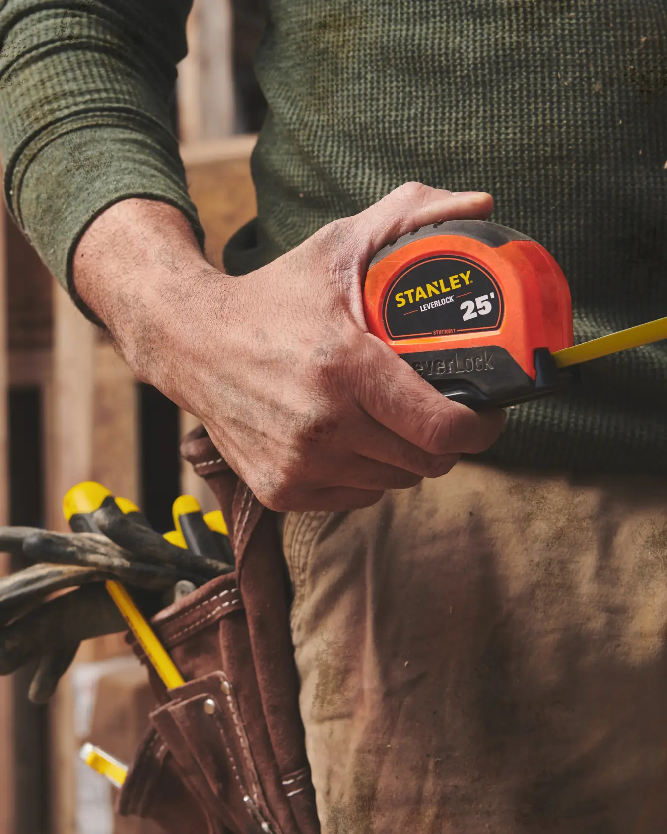 STANLEY STHT30817S 25-foot tape measure held by person in work clothes with tool belt outdoors.