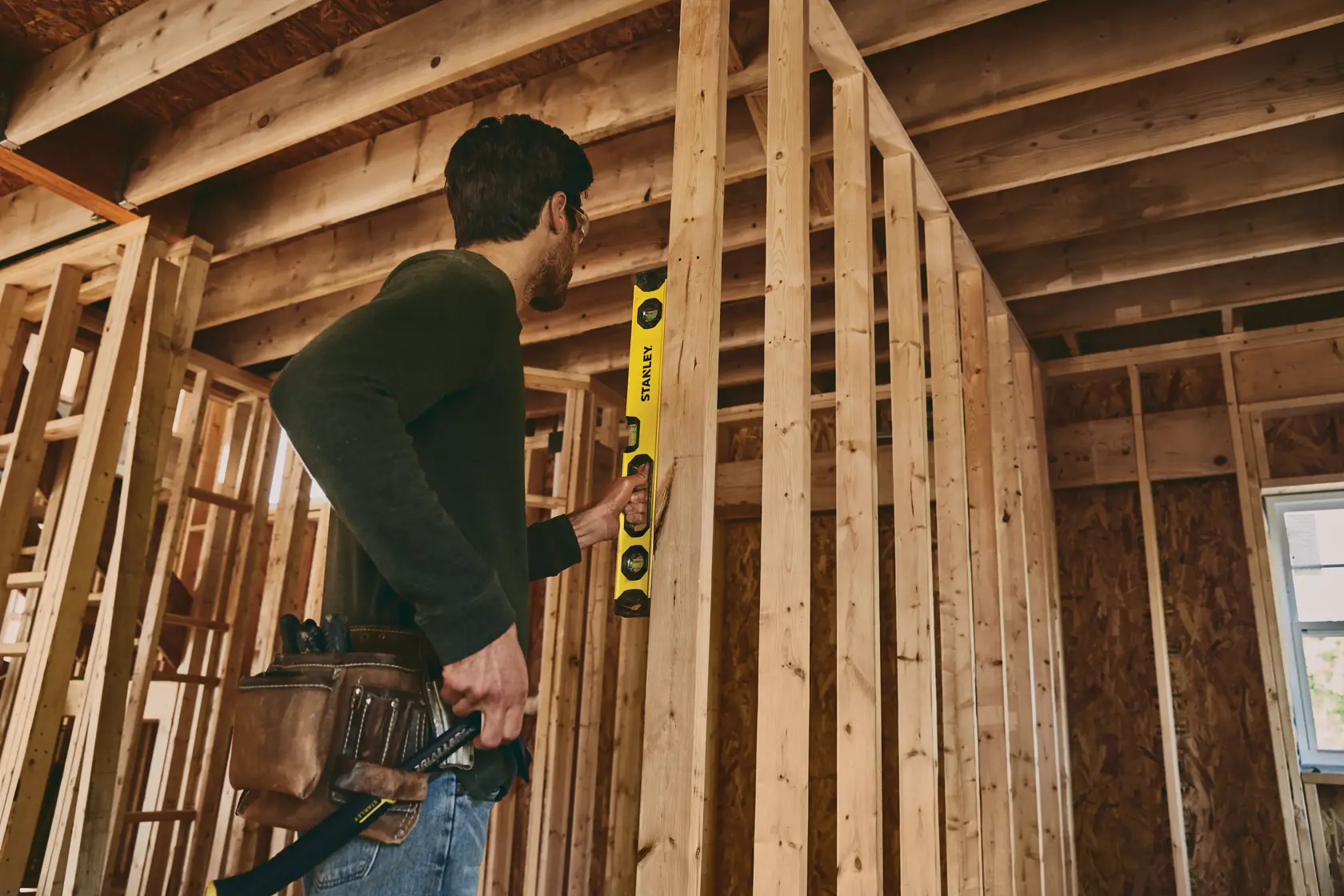 STANLEY STHT42496 level held by a person checking vertical alignment of wall studs in a wooden frame construction.