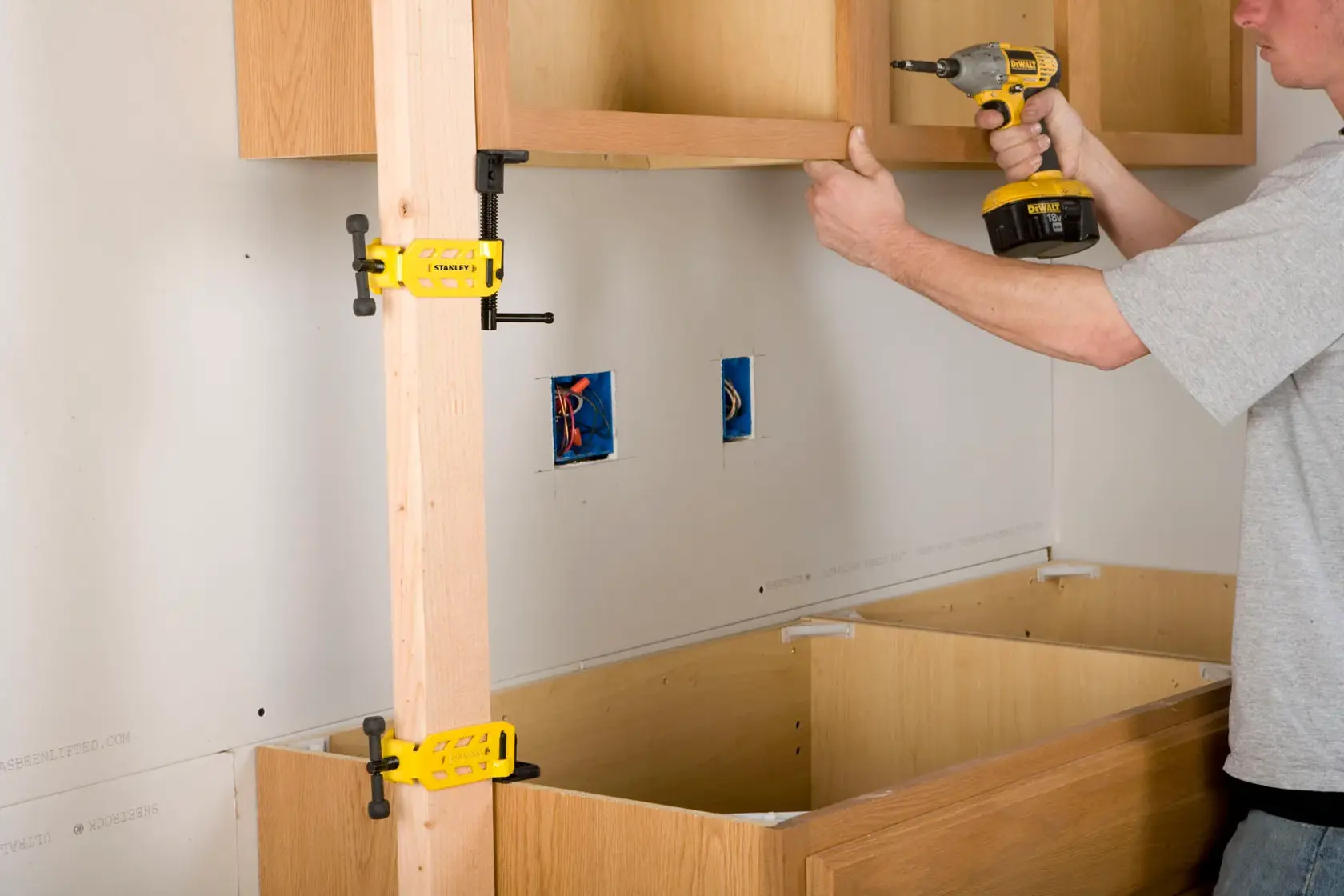 STANLEY STHT83166 clamp holding wooden frame during cabinet installation, side angle photo.