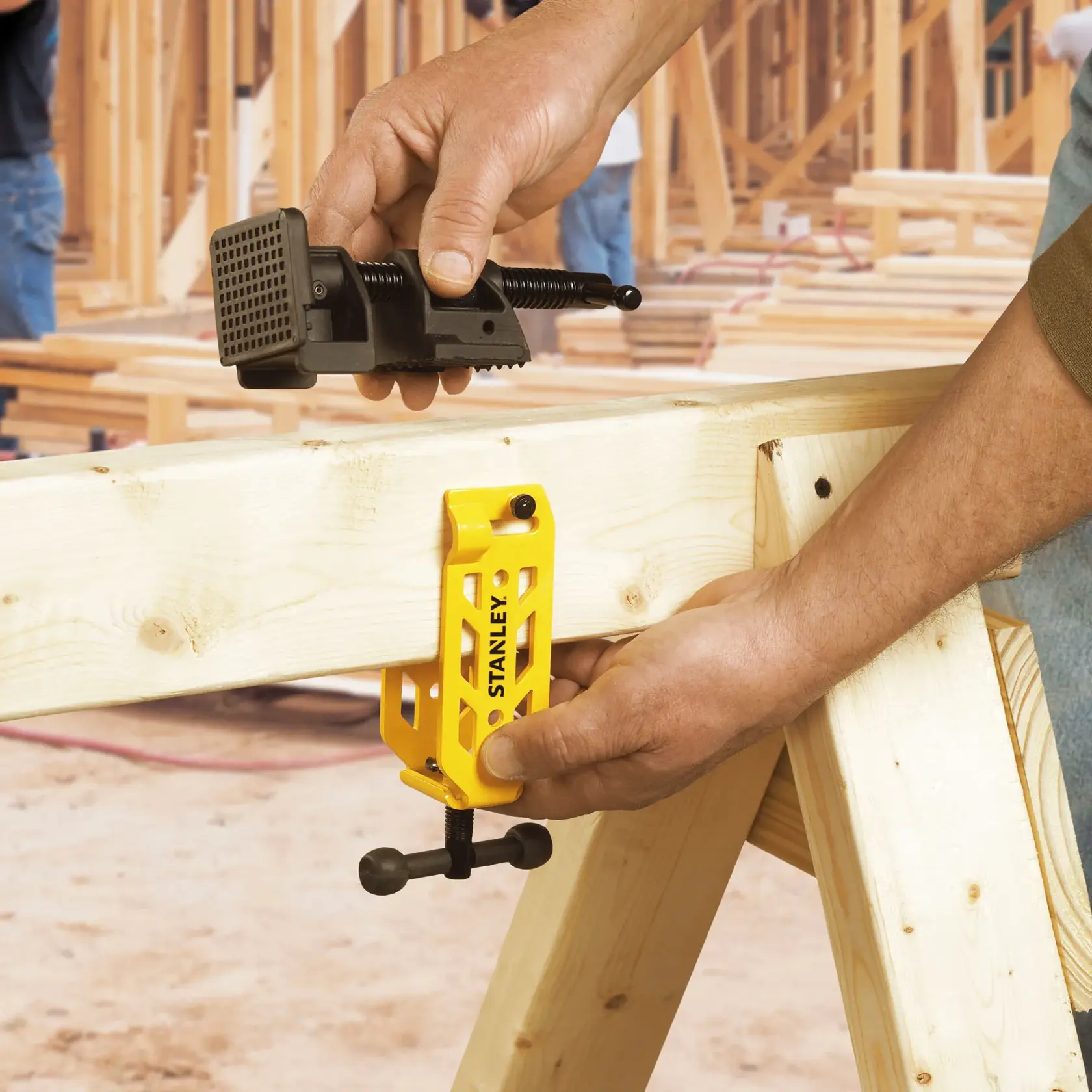 STANLEY STHT83166 yellow woodworking clamp in use on wooden beam at construction site, close-up.