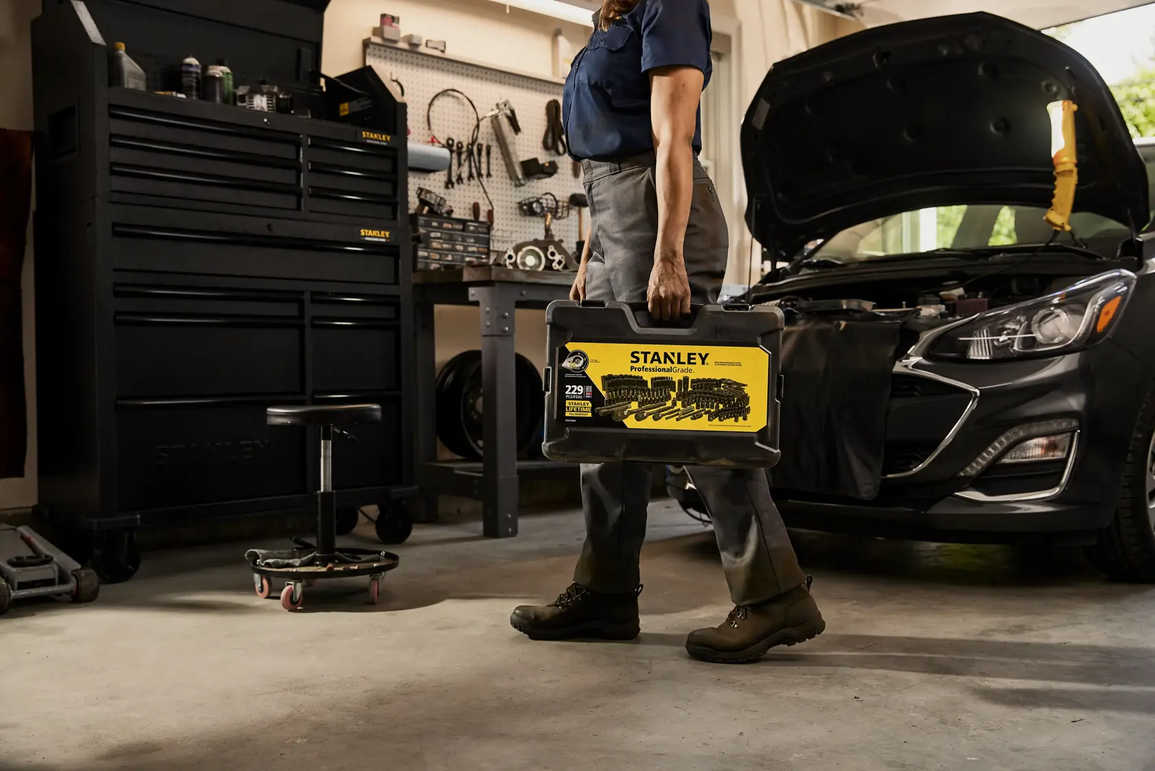 Photo of a person holding a STANLEY STMT75064 tool set case in a garage with a car and tool chest in the background.