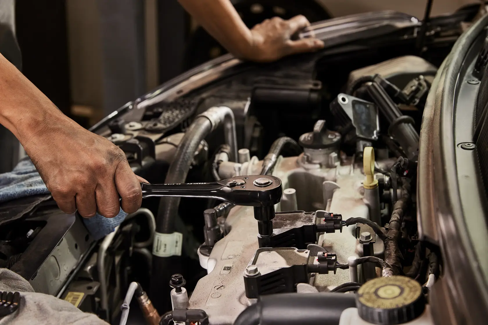 Photo of a hand using a STANLEY STMT75064 ratchet wrench on a car engine, close-up view.