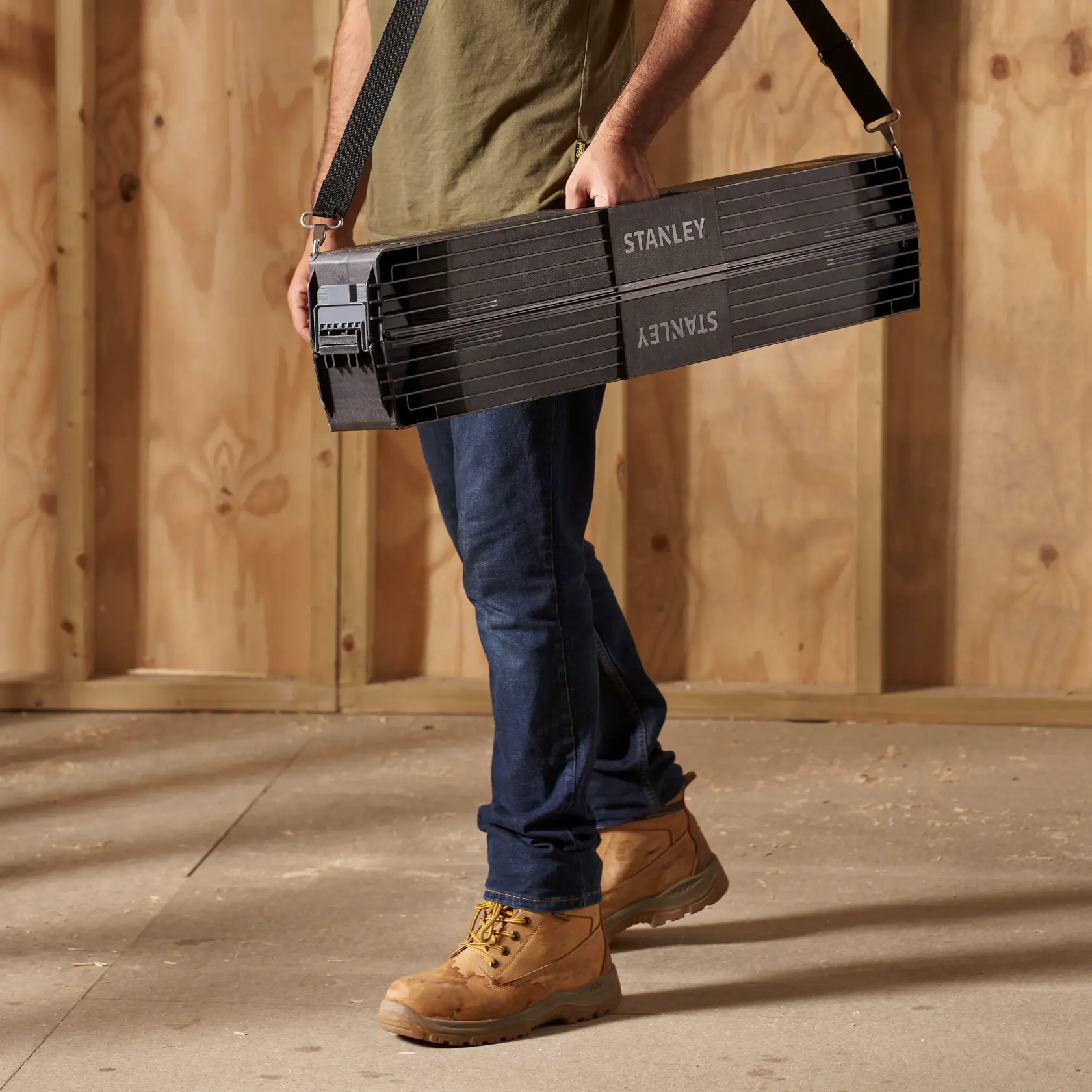 Photo of STANLEY STST11151 portable black sawhorse carried with shoulder strap, shown in workshop setting.
