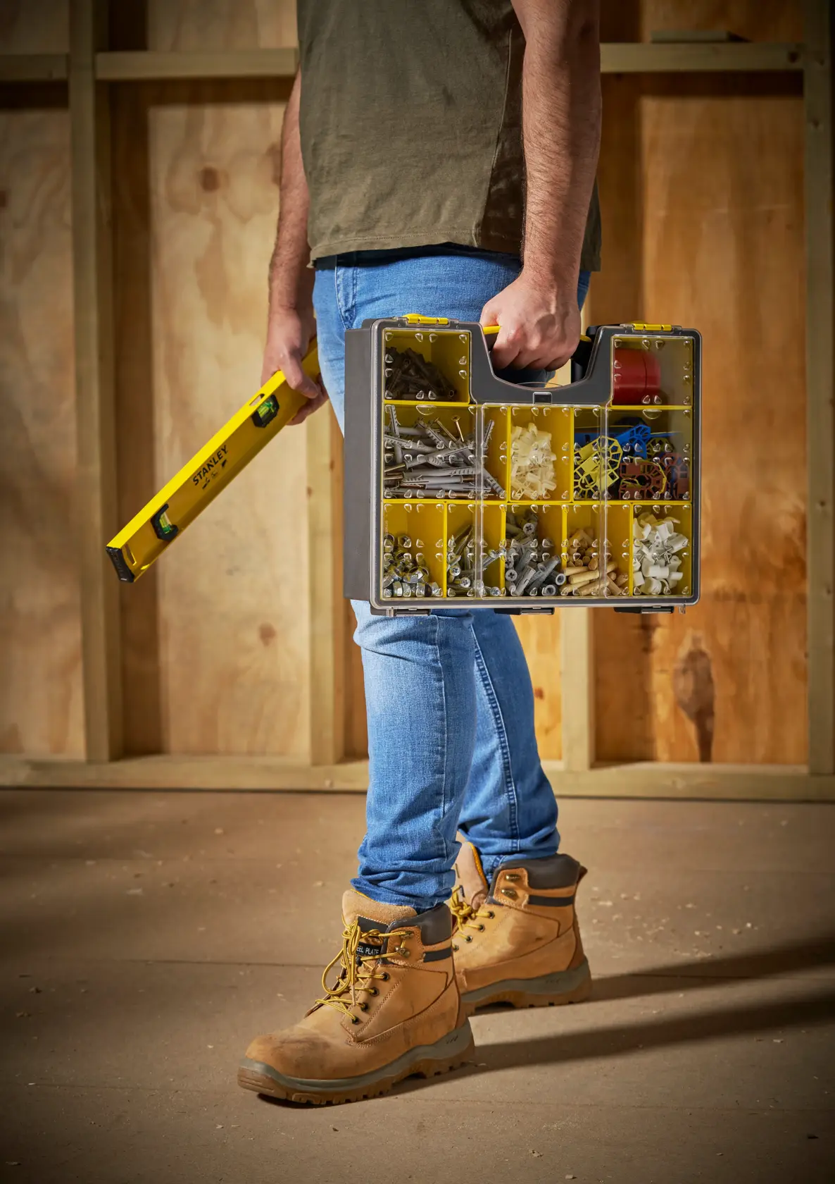 STANLEY STST14710 organizer box with clear lid, yellow compartments, carried by person in work boots, side view.