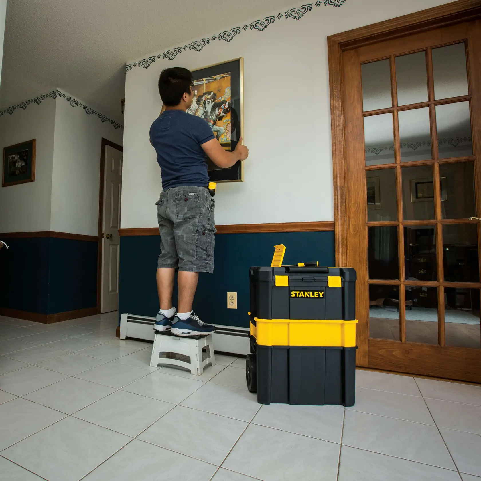 Photo of STANLEY STST18631 black and yellow rolling tool box in a home interior near a person hanging a picture.