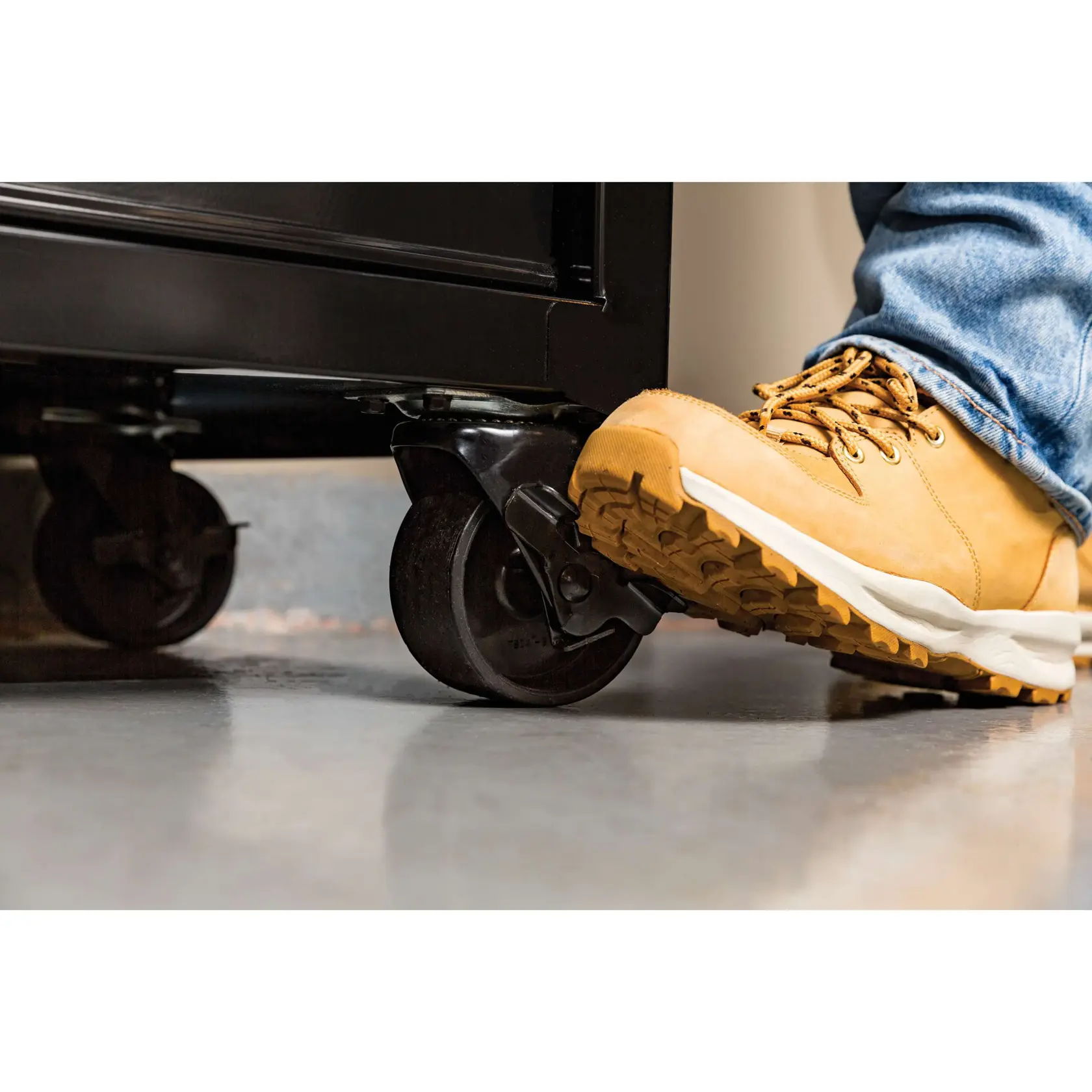 STANLEY STST23151BK storage cart caster wheel with brake, close-up side view, foot pressing brake lever.